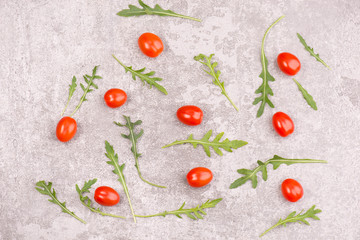 Red cherry tomatoes and fresh arugula leaves on a grey textured stone background, empty copy space