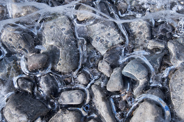 Natural winter background of frozen pebbles and hoarfrost crystals over river ice