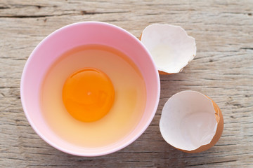 The brown chicken eggs in a pink bowl and a wooden table as a background.