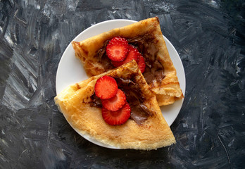 Fresh pancakes with chocolate paste and strawberry on gray background. Top view. Russian style pancakes for Pancake Week. 