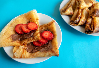 Fresh pancakes with chocolate paste and strawberry on blue bright background. Russian style pancakes for Pancake Week. English wrapped pancakes. 