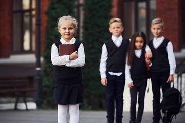 Group of kids in school uniform posing to the camera outdoors together near education building