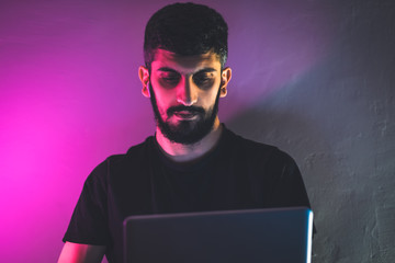 Man freelancer is working with a laptop in a room with colored lighting. Remote work concept