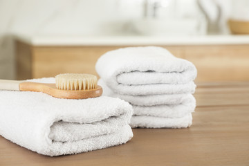 Stack of clean towels and massage brush on wooden table in bathroom