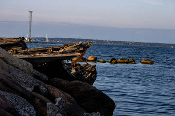 A broken boat at the wharf amid the opposite coast; The boat is stuck with chips and metal rivets