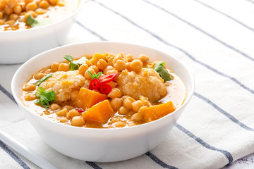 Curry with chickpeas, pumpkin, zucchini and cauliflower in white bowls on the table. Vegetarian curry with stewed vegetables. Traditional indian cuisine, vegan food.