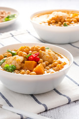 Curry with chickpeas, pumpkin, zucchini and cauliflower in white bowls on the table. Vegetarian curry with stewed vegetables. Traditional indian cuisine, vegan food.