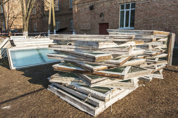 A lot of old wooden windows in the garbage outdoors near building, replacing with new pvc.