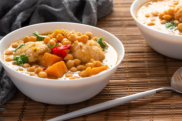 Curry with chickpeas, pumpkin, zucchini and cauliflower in white bowls on the table. Vegetarian curry with stewed vegetables. Traditional indian cuisine, vegan food.