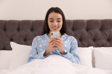 Young woman addicted to smartphone in bed at home