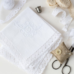 Needlework. Two white handkerchiefs with lace trim, pillow for needles, scissors, lace and a thimble on a light background. Selective focus.