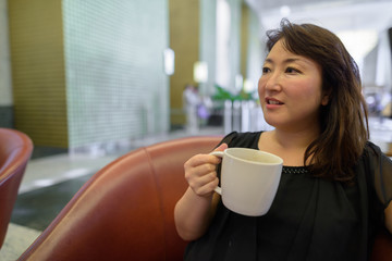 Mature beautiful Asian woman relaxing inside the coffee shop