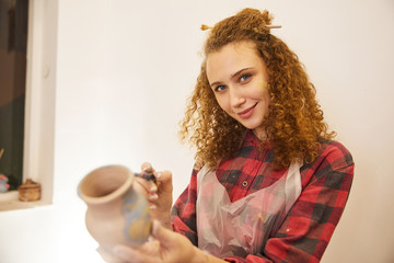 Pretty curly girl smiling paints a vase