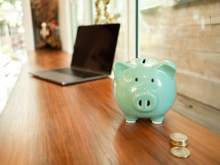 Blue piggy bank on the table with laptop and a cup of coffee.