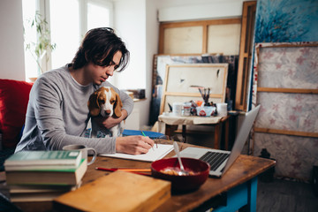 young man cuddling with his dog while working in his room
