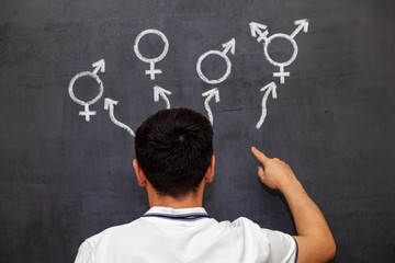 A man makes a choice at a chalk Board with gender symbols. A symbol of transgender and female and male gender symbols on a chalkboard.