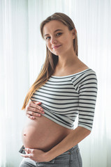 Happy pregnant woman with big belly by the window. Concepts of pregnancy and family