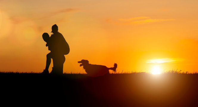 Silhouette of a couple in love at sunset. girl and guy are playing next to dog running.