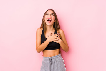 Young caucasian fitness woman posing in a pink background laughing keeping hands on heart, concept of happiness.