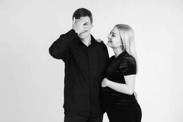 Pregnant woman and her husband smiling in black clothes on a white background. Black and white picture. Beautiful married couple. Copy, empty space for text