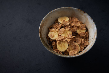 Bowl of granola with banana. Concept for a tasty and healthy meal. Dark stone background. Close up. Copy space. 