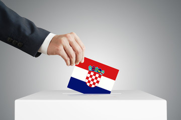 Man putting a voting ballot into a box with Croatian flag.