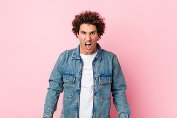 Curly mature man wearing a denim jacket against pink background screaming very angry and aggressive.