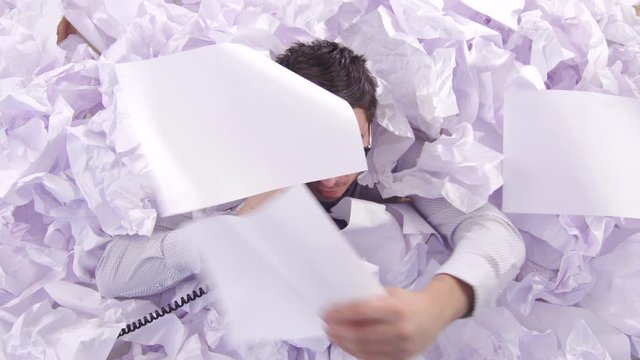 confused man office worker is talking on the phone in a large heaps of paper