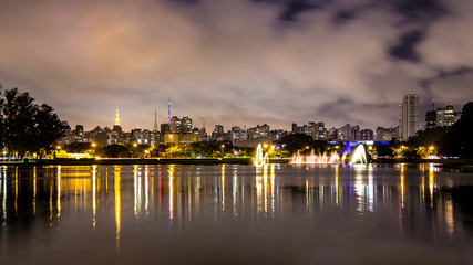 Evening Illuminations Light In Sao Paulo, Brazil. Night Illuminated Ibirapuera Park. Modern Skyscrapers, Reflection On The Lake And Water Fountain. Miracle Lights Of Metropolis City At Night.