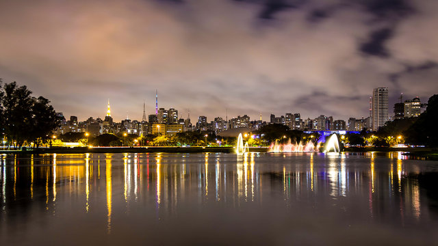 Evening Illuminations Light In Sao Paulo, Brazil. Night Illuminated Ibirapuera Park. Modern Skyscrapers, Reflection On The Lake And Water Fountain. Miracle Lights Of Metropolis City At Night.