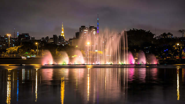 Illuminated Ibirapuera Park At Night. Modern Skyscrapers, Reflection On The Lake And Floating Fountain. .High Water Jets, Miracle Lights Of Metropolis City, Sao Paulo, Brazil.