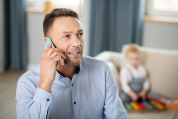 Bearded man in a blue shirt looking interested while speaking on the phone