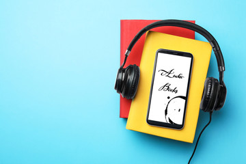 Books with modern headphones and smartphone on light blue background, top view