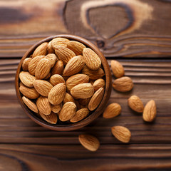 Top view of a wooden bowl with almonds on wood