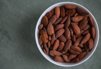 Almonds in a white bowl on a textured green background, top view. Copy space on left side.