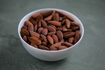 Almonds in a white bowl on a textured green background.