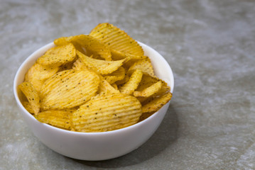 Potato chips in a bowl on a light background, top view.