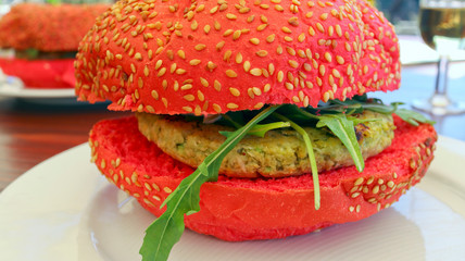 Fast food on a plate, vegetarian burger topped with rocket leaves, served in red wheat bun covered with sesame seeds.