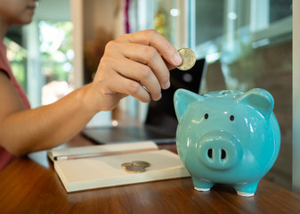 A hand putting a coins in to blue piggy bank. To encourage for saving money