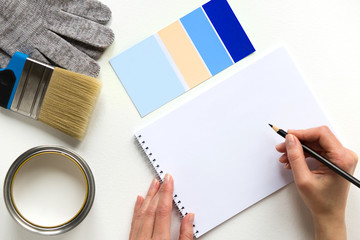 Paint color chart sample swatches, gloves, notebook and woman hand with pencil, paint brush and tin of paint. Concept choice color and design project