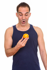 Mature handsome Persian man holding orange ready for gym