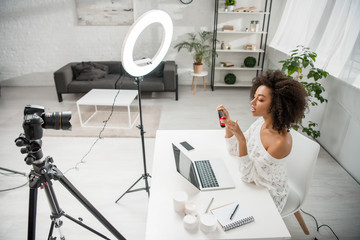 african american influencer holding hair straightener near digital camera and gadgets
