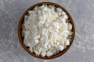 Cottage cheese in a wooden bowl on a light gray background.