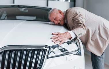 Cheerful aged man in formal wear stands in front of modern white car