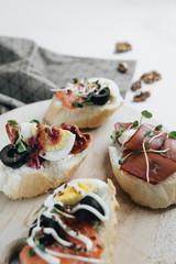 Delicious fresh bruschettas with eggs, salmon, olives and meat , traditional Italian cuisine, ingredients on white  table