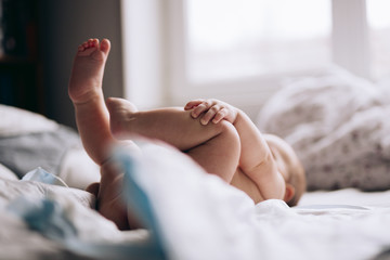 Infant Baby on bed. Nude naked legs feet and bud. Free space. Baby infant care. Inside. No face. 