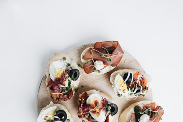 Delicious fresh bruschettas with eggs, salmon, olives and meat , traditional Italian cuisine, ingredients on white  table