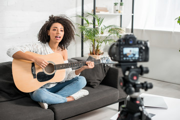 selective focus of young african american girl in braces playing acoustic guitar and singing near digital camera