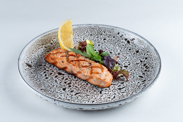 Grilled salmon steak with greens and lemon isolated on white background