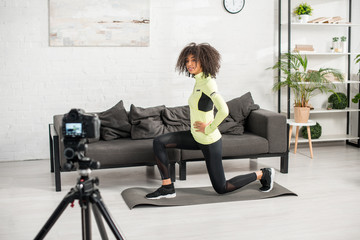 selective focus of happy and curly african american video blogger in braces exercising near digital camera